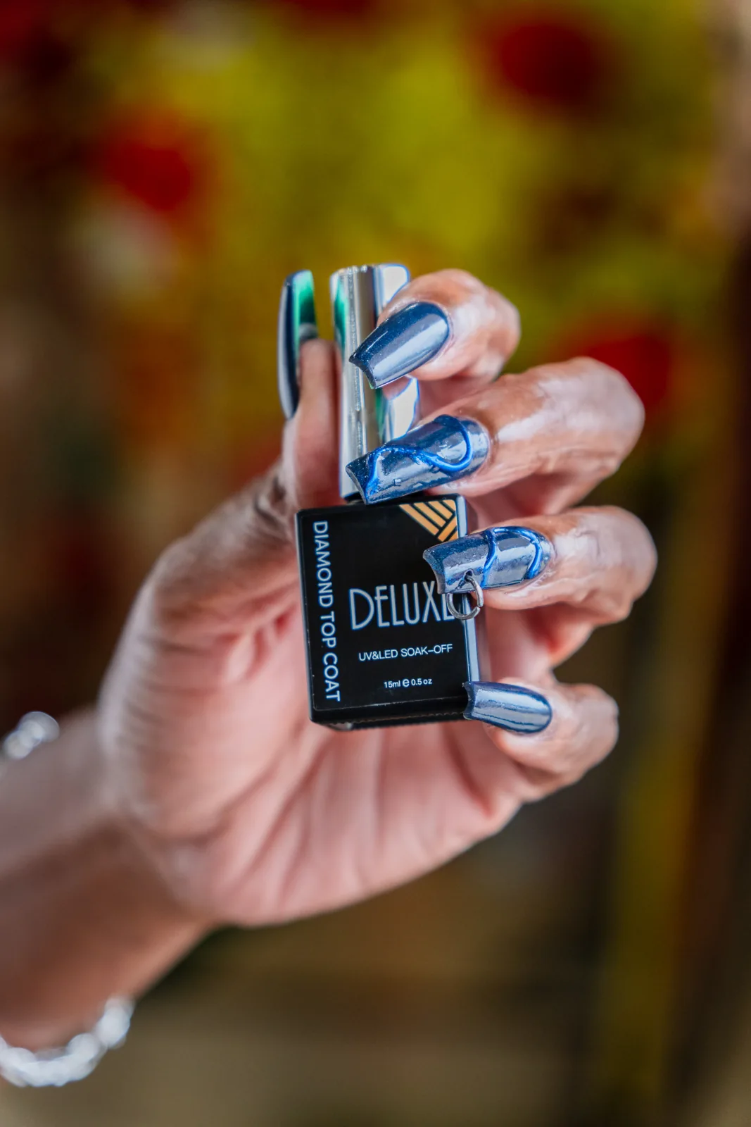 Reflective blue chrome nails holding a Deluxe top-coat bottle